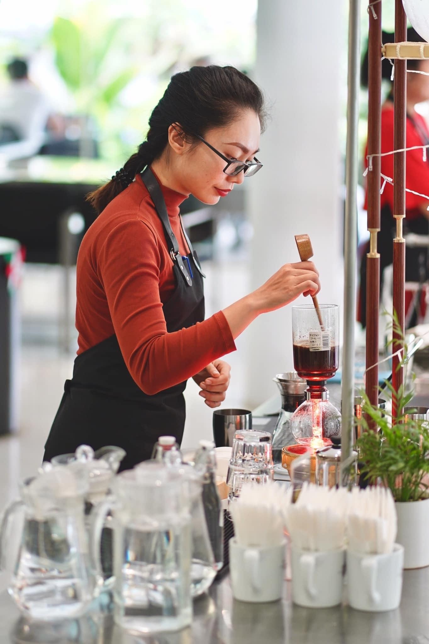A barista carefully preparing coffee with a siphon brewer.